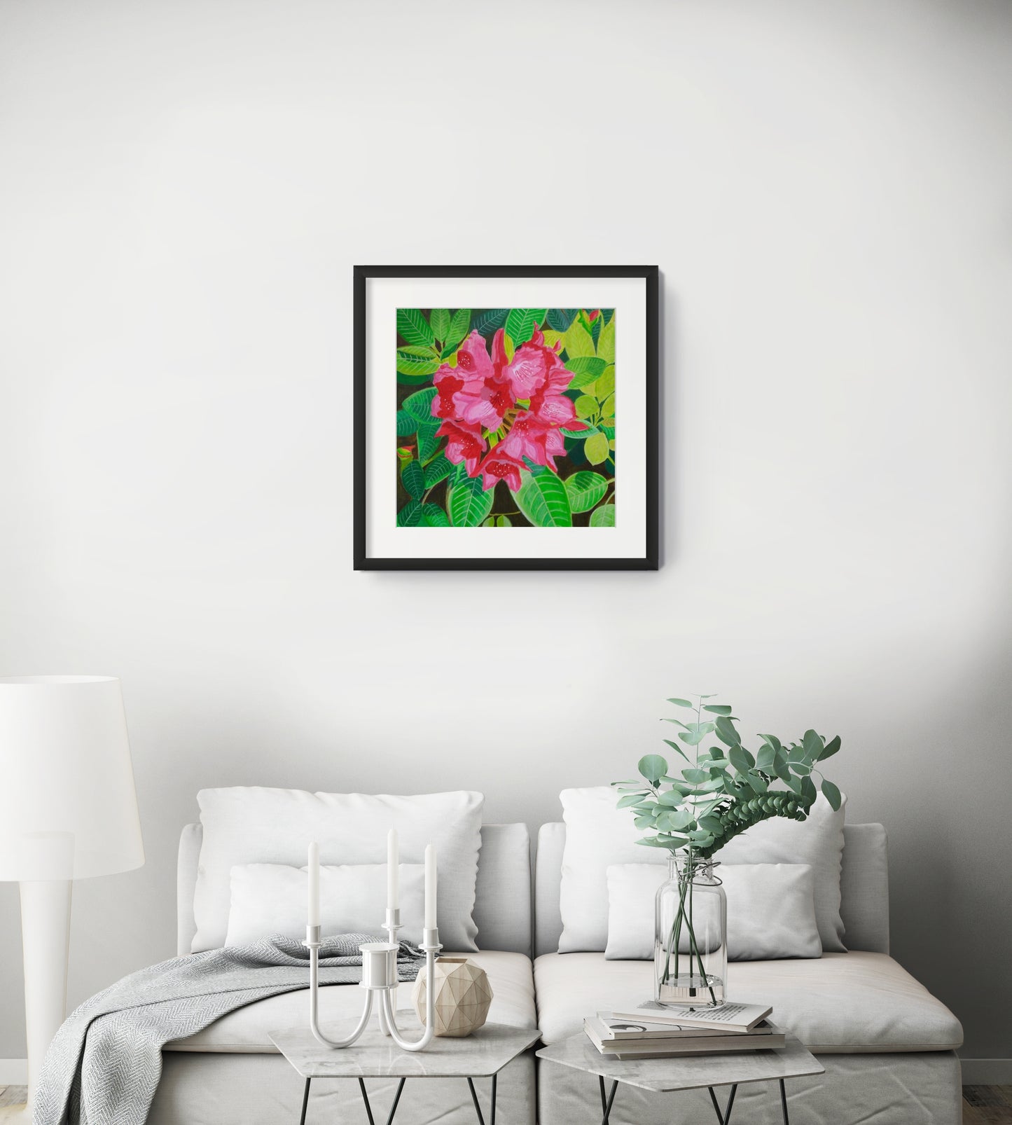 Éclat de Rhododendron fine art floral print by Nelleke Bruno displayed above a white sofa in a modern living room, presented in a black frame with a white mat board.
